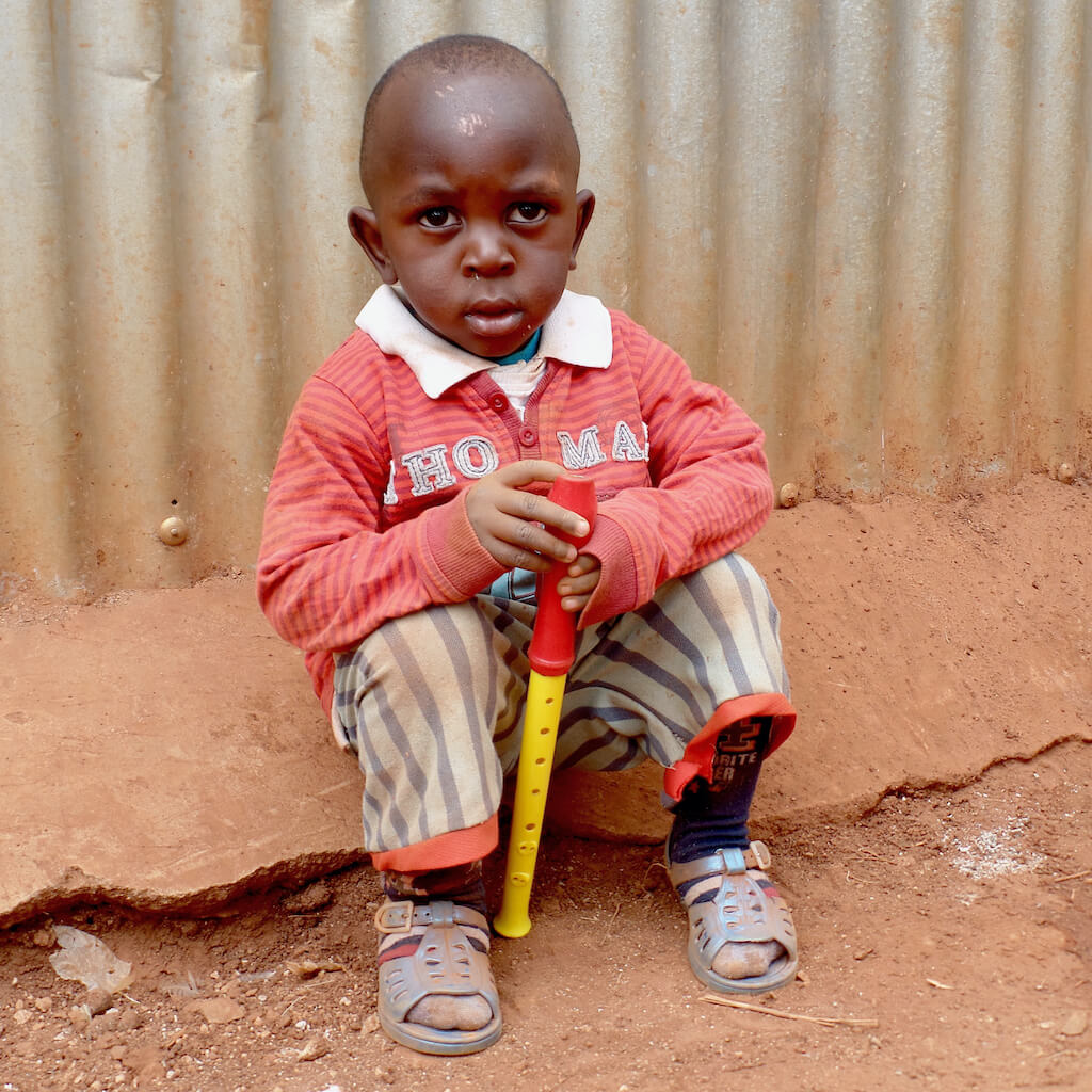 Child sitting on dirt ground with musical instrument